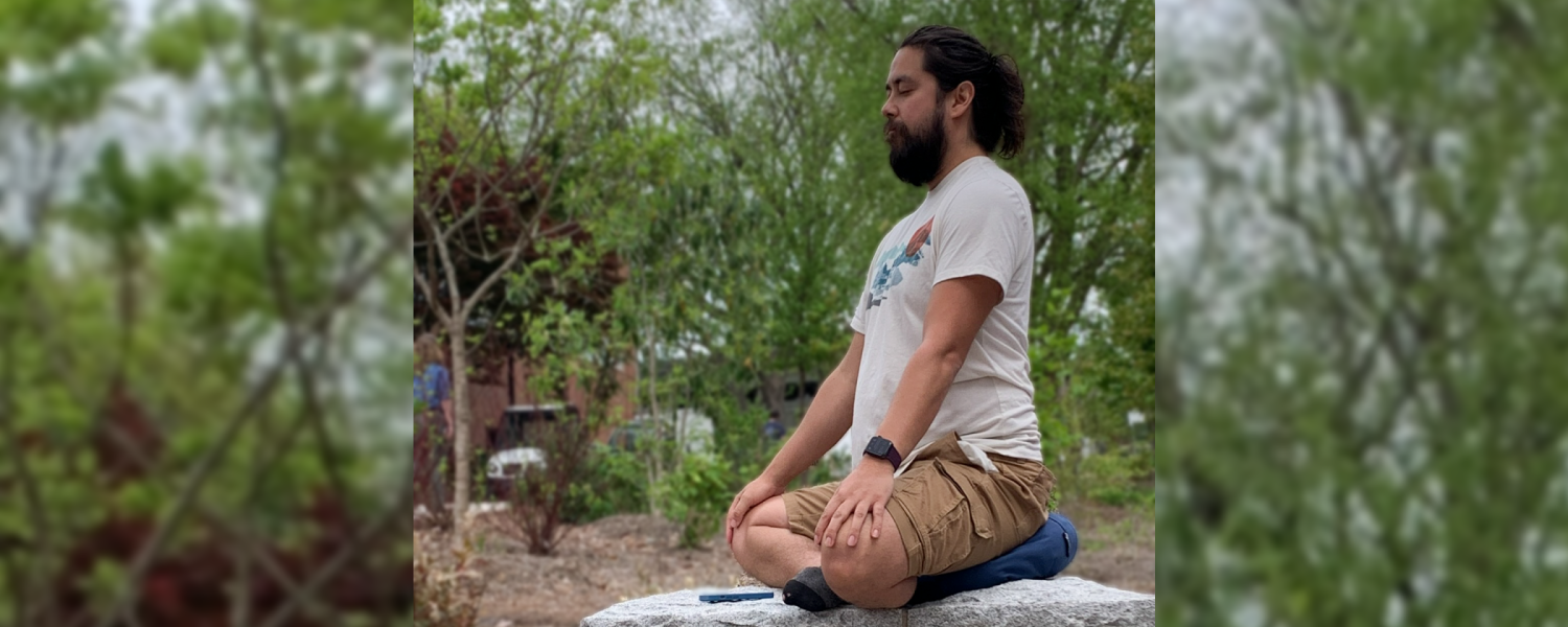 A man sits on a stone ledge, his legs crossed in a yoga position.