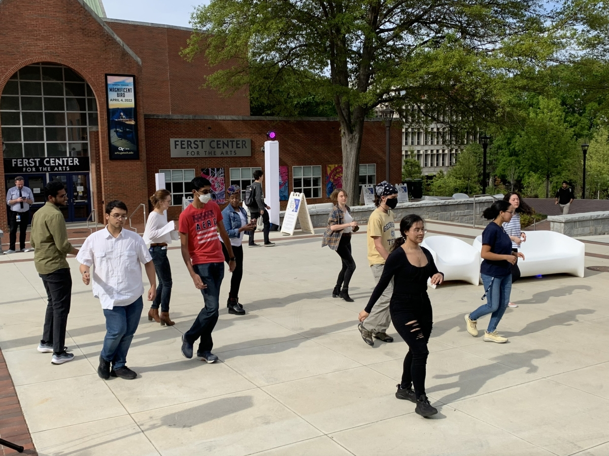 A woman dressed in black stands in front of a group of people, teaching them how to dance salsa.