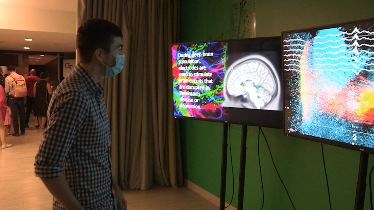 A man stands in front of two video monitors displaying visual representations of brain waves.