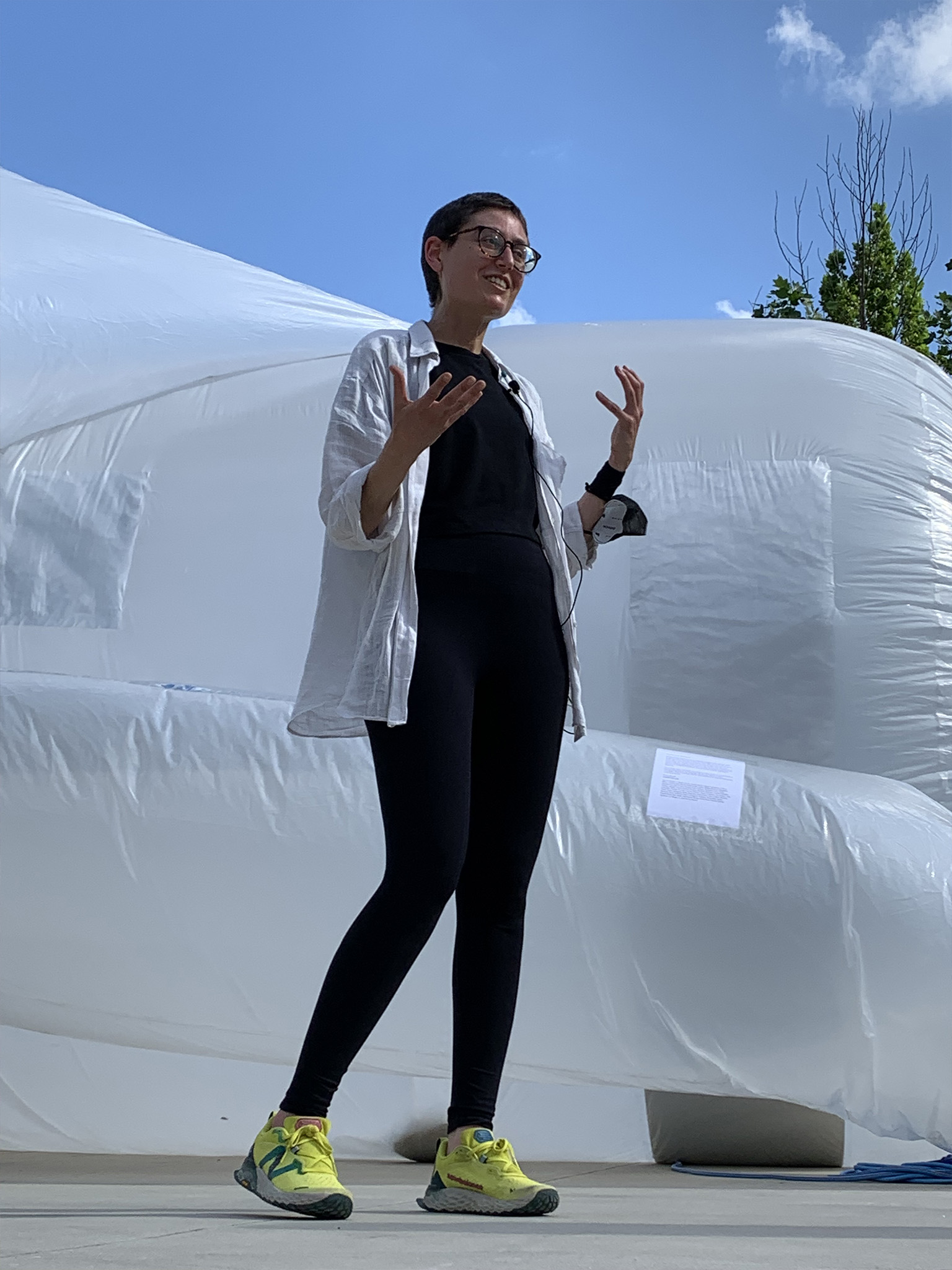A woman wearing black with a white jacket stands in front of a white inflated structure