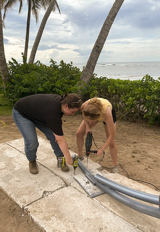 Danielle and Elizabeth screw the base of the sculpture to the cement floor.
