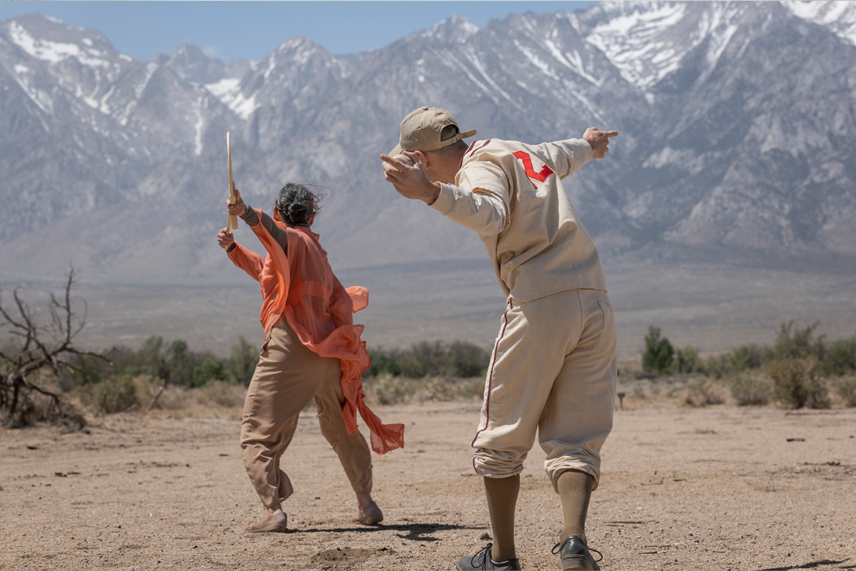 Two figures facing away from the camera, mid-motion. Behind them is a range of mountains.