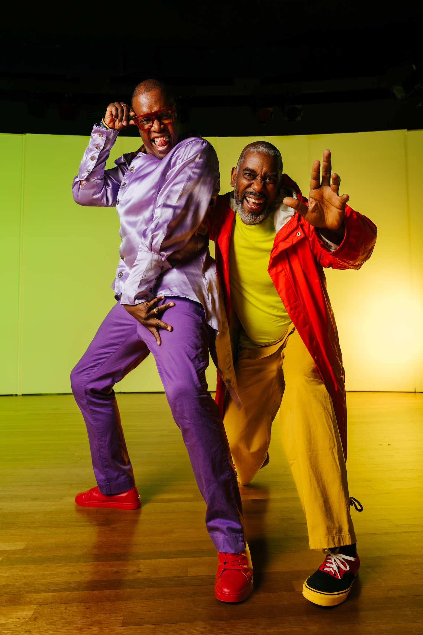 Two people on stage looking at camera wearing bright clothing with bright background