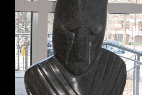 sculpted and polished black stone, a human face with eyes cast down and upper torso