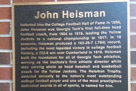 Plaque reading: Inducted into the College Football Hall of Fame in 1954, John Heisman was Georgia Tech's first full-time head football coach, from 1904 to 1919, leading the Yellow Jackets to a national championship in 1917. In 16 seasons, Heisman produced a 102-29-7 (.764) record, including the most lopsided victory in college football history, a 222-0 win over Cumberland in 1916. Heisman built the foundation for all of Georgia Tech athletics, serving as the Institute's first athletic director...
