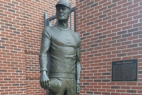 Standing figure of John Heisman, his right hand holding a bullhorn resting on his right thigh.