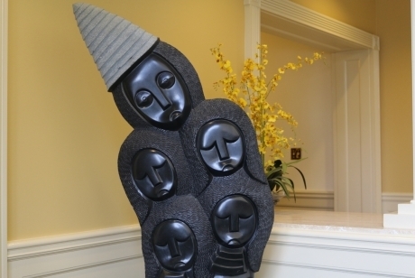 Five carved faces in smooth black finish with conical hat in gray textured finish. Hair surrounding faces is textured in a convex pattern as well