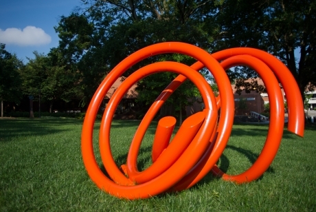 Bright orange steel tubing in a twisted circular pattern on its side in the grass.