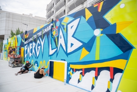 A seven-foot high wall is painted in vibrant colors, with images referencing energy sources. The text reads "welcome to the smart energy lab."
