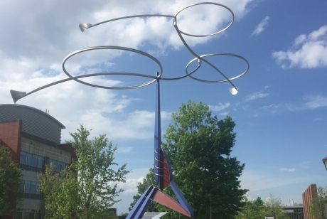 A center pole of colored metal with angular protrusions, in a cement base, topped by polished silver circles that move with the wind