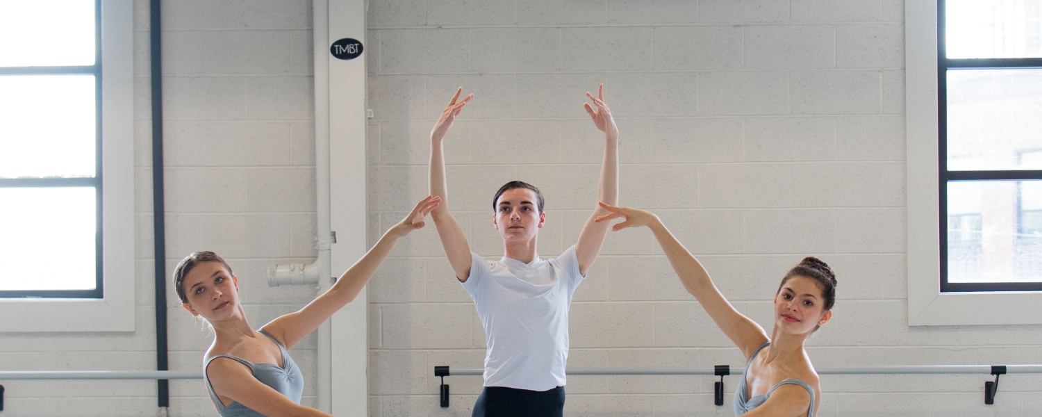 Four dancers are posed as a classical quartet. The three women wear pale blue leotards with gauzy white skirts. The man wears a white T shirt and black tights. 