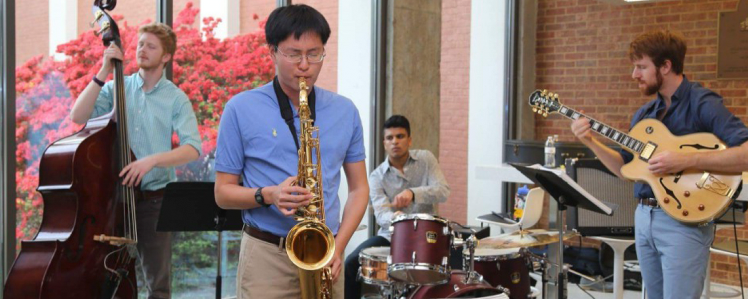 Three male musicians each playing the bass, saxophone, electric guitar, and drums.