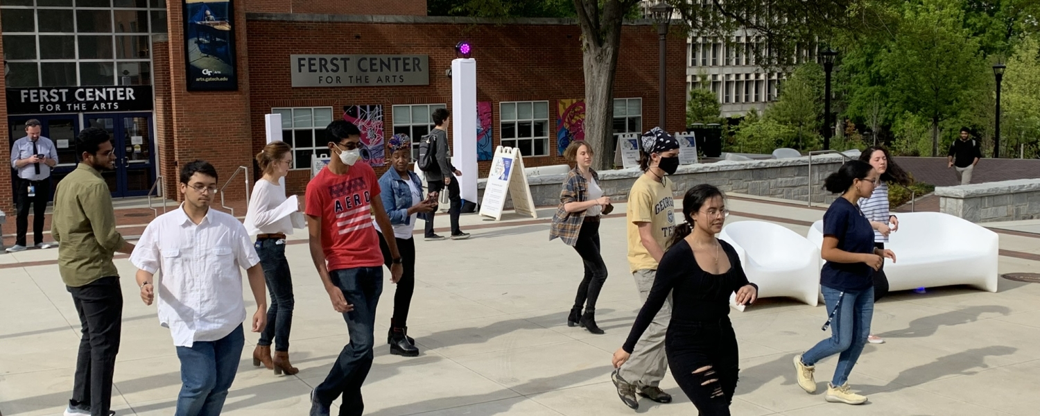 A woman dressed in all black stands in front of a group of students to teach them how to dance, by GT Salsa student organization.