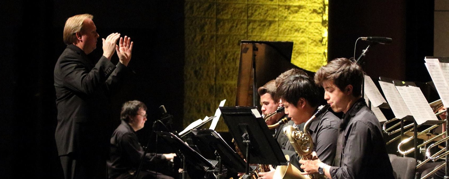 Photo of musicians playing instruments while conductor stands in front