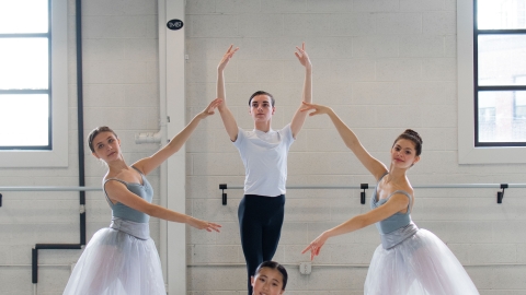 Four dancers are posed as a classical quartet. The three women wear pale blue leotards with gauzy white skirts. The man wears a white T shirt and black tights. 