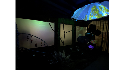 a dark room with video projections, animatronic objects, and an upside down umbrella displaying video of a blue sky and trees