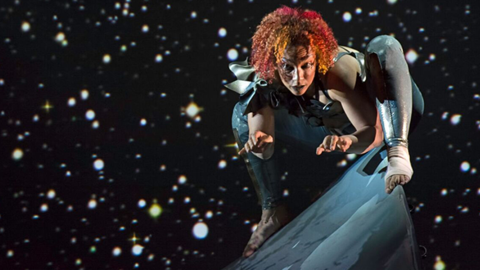 Andromeda perches out of her wheelchair on the sharp peak of the ramp. From atop of this mountain, she looks directly into our eyes. Her hair is flame red; a constellation of stars sparkles behind her. Photo: BRITT/Jay Newman 