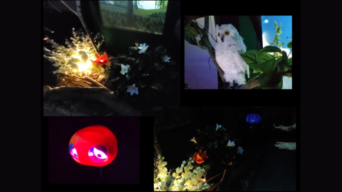 A dark room with video projections, animatronic objects, and an upside down umbrella displaying video of a blue sky and trees.
