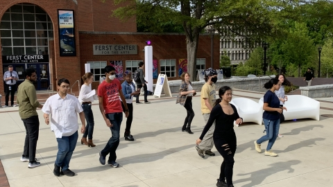 A woman dressed in all black stands in front of a group of students to teach them how to dance, by GT Salsa student organization.