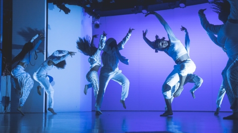 Several dancers on stage wearing white with blue and purple lighting