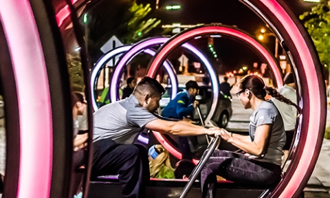 Two people are sitting facing each other inside a large circular frame with their hands on a push bar between them
