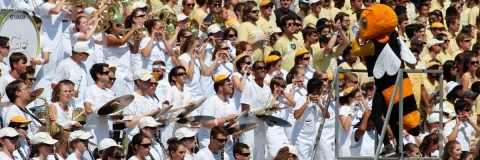 student musicians wearing either white or gold t-shirts are on a bandstand, being conducted by Buzz, the Georgia Tech mascot