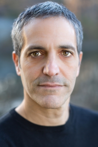 A man with close cropped grey hair stares directly at the camera.