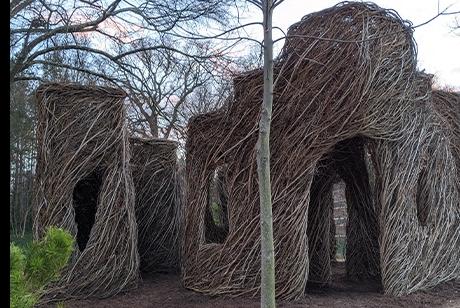 Thin saplings and branches have been woven together in the shape of cube-like buildings with arched doors and window