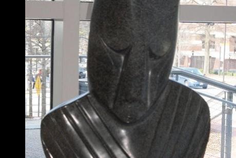 sculpted and polished black stone, a human face with eyes cast down and upper torso