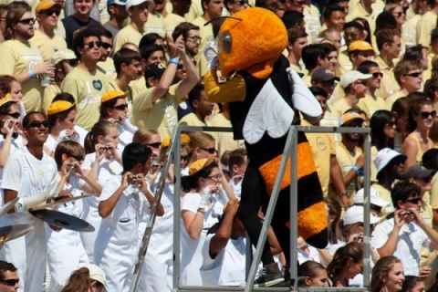 student musicians wearing either white or gold t-shirts are on a bandstand, being conducted by Buzz, the Georgia Tech mascot