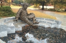 Bronze figure of Albert Einstein, reclining on marble steps with papers in his lap, reflecting on the map of the sky engraved in the ground below him.