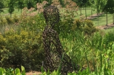 seated figure, made of bronze lattice, in a field of grasses and bushes