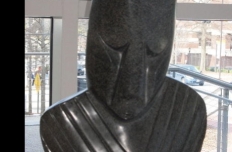 sculpted and polished black stone, a human face with eyes cast down and upper torso, no arms