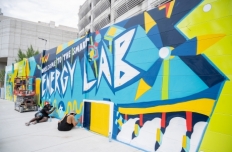 A seven-foot high wall is painted in vibrant colors, with images referencing energy sources. The text reads "welcome to the smart energy lab."