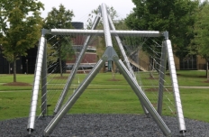 Shiny metal tubing in overlapping shapes with webs of metal stretched from pole to pole, viewed from the back