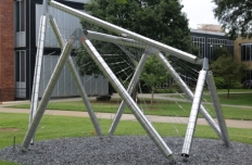 Shiny metal tubing in overlapping shapes with webs of metal stretched from pole to pole, viewed from the side