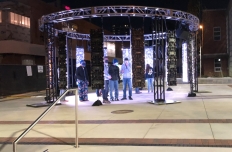12 LED panels, each 8 feet tall, are hanging from a truss arranged facing eachother in a circle. People are standing within and around the screens.