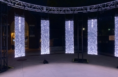A close up of four of the 12 glowing LED panels hung from a truss in a circle, each displaying scattered white points of light