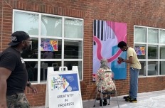 People stand outside at the wall of a building, painting on the canvasses installed between the windows. ARTiculate ATL and SMILE GT mural installation