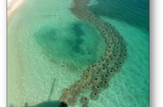An aerial view of an artificial reef visible through crystal clear teal blue ocean