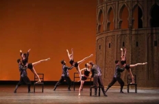 A ballet company on stage. Five couples in various poses, some using a chair as a prop