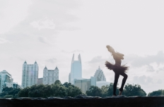 a woman in a dark colored tutu arching her back, seen in profile against the Atlanta skyline