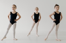 three young girls in black leotards and tights, hands on hips and right leg extened out to the side.