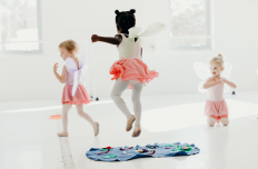 three little girls in dance skirts and leotards and tights are jumping and running in a dance studio