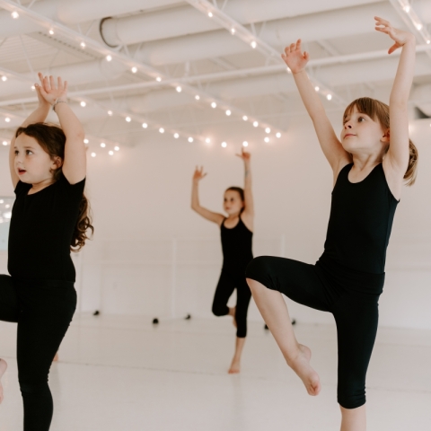 Students in black clothing balancing on one leg with two arms lifted above their heads